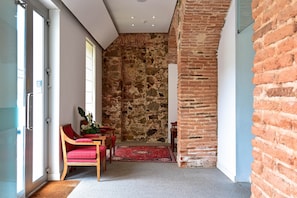 Une pièce avec un mur en pierre, une chaise en bois avec un coussin rouge et un tapis rouge sur le sol.