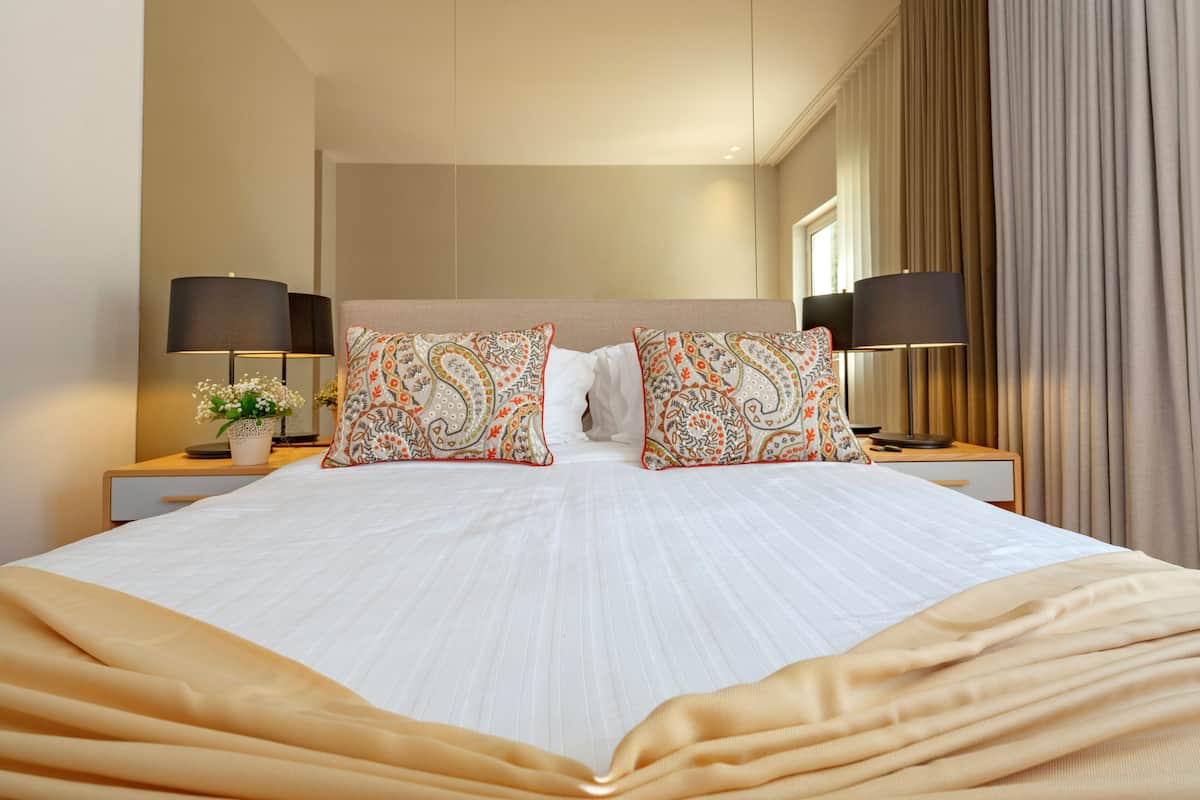 A hotel room with a large bed, two nightstands, two lamps, and a window with curtains.