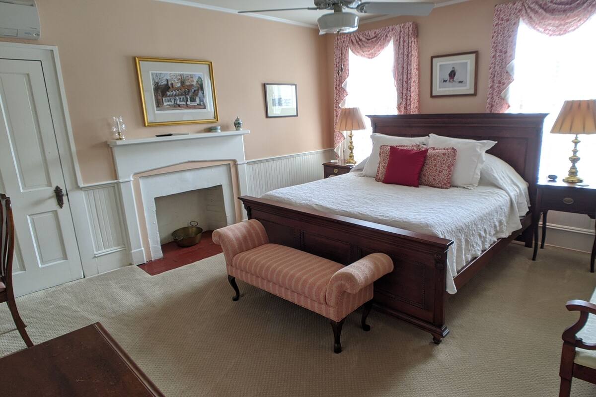 A bedroom with a large bed, a fireplace, a bench, and a mirror.
