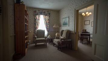 A cozy living room with a wooden bookshelf, patterned wallpaper, and a dining area with a chandelier.