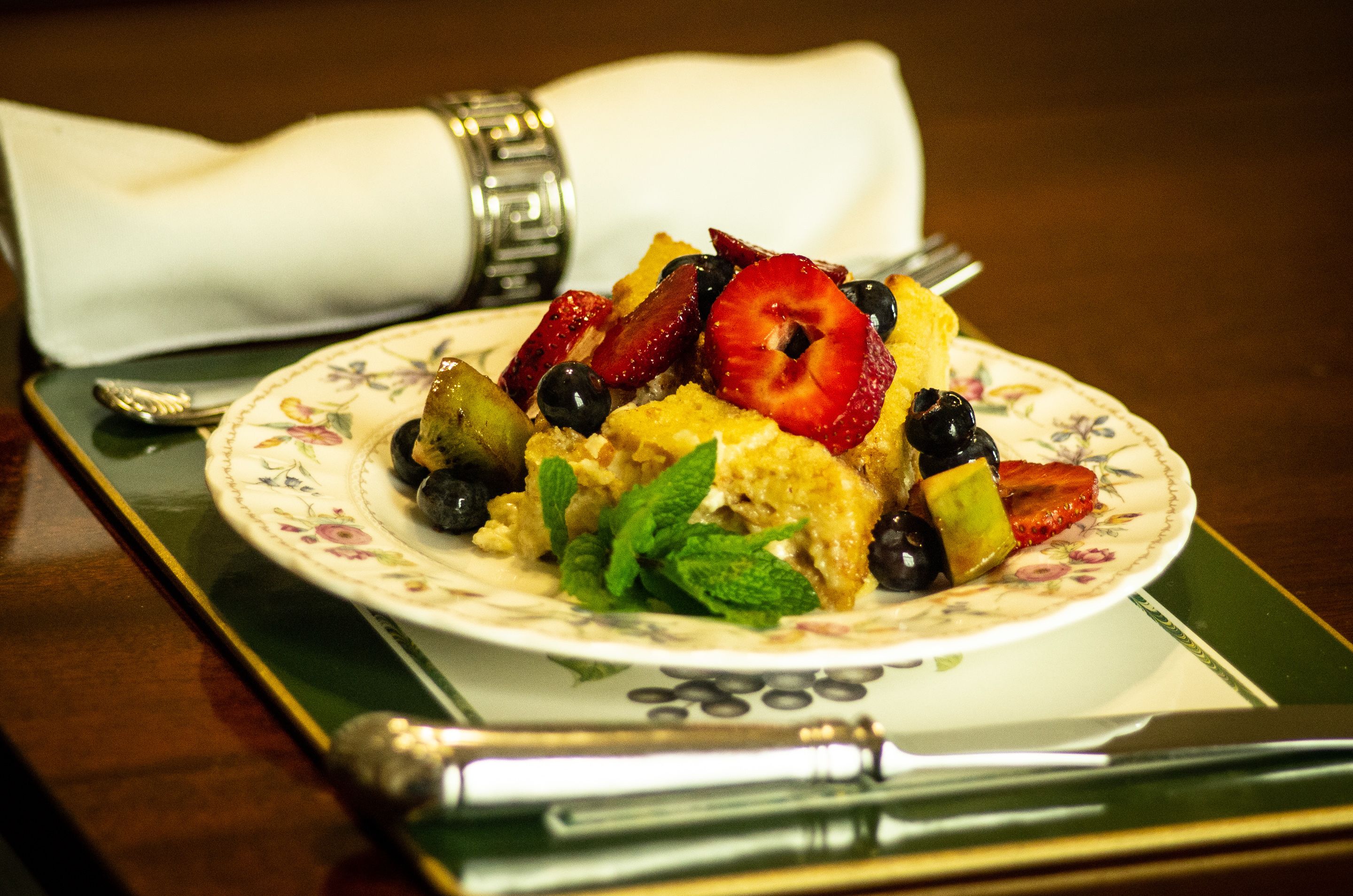 A plate of food with strawberries, blueberries, and mint leaves on a floral-patterned plate.