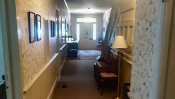A hallway with a carpeted floor, framed pictures on the walls, a lamp, and a staircase.