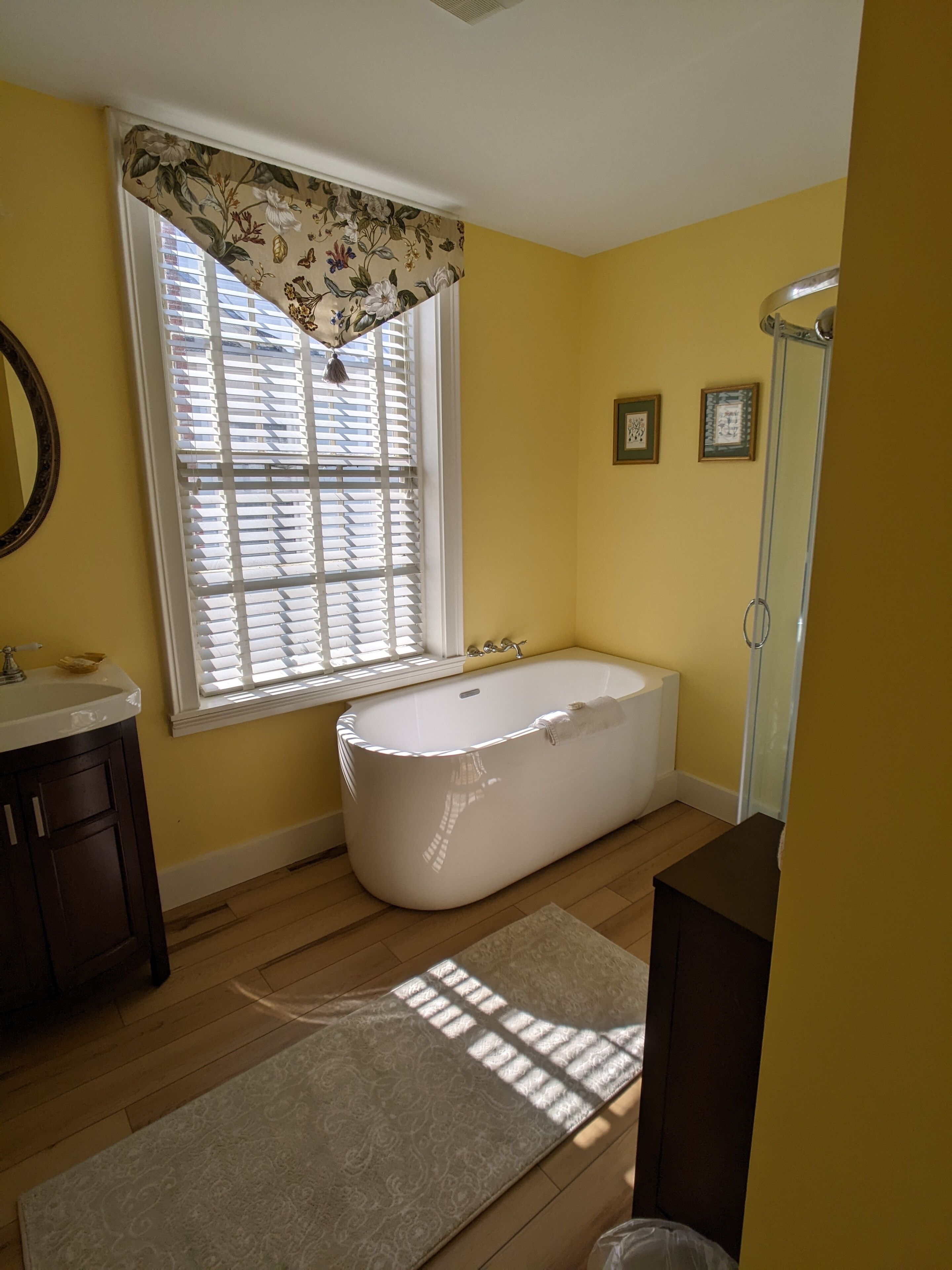 Un baño con bañera independiente, una ventana con persianas, un lavabo y un espejo.