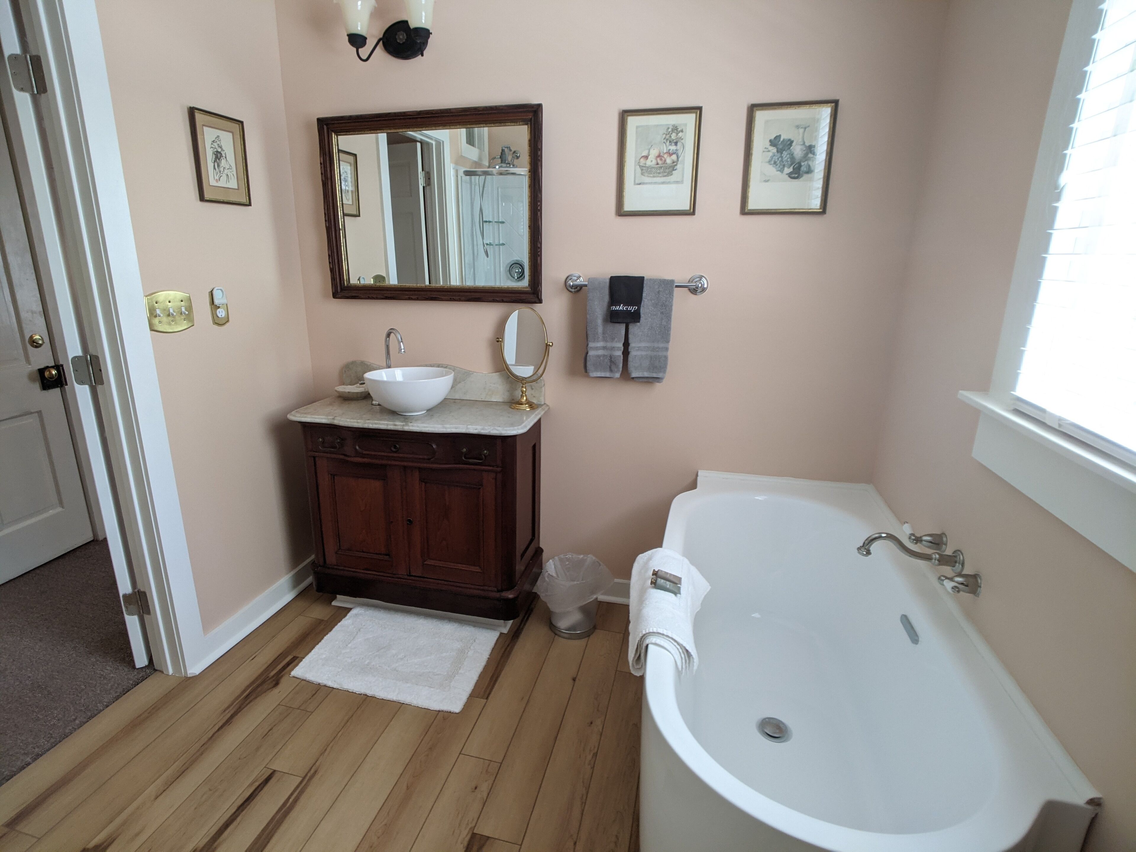 A bathroom with a wooden vanity, a white sink, a large mirror, and a bathtub.