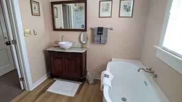 A bathroom with a wooden vanity, a white sink, a large mirror, and a bathtub.