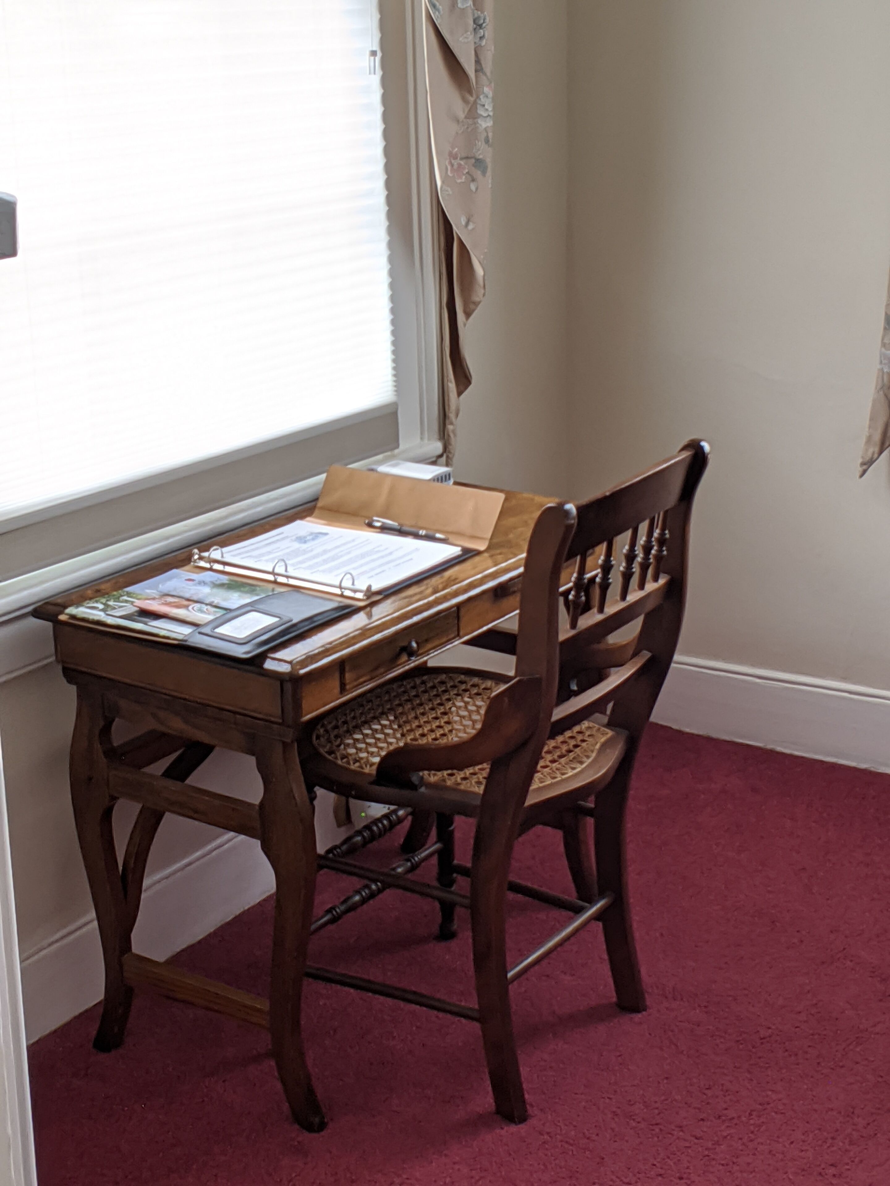 A wooden desk with a chair, papers, and a pen.