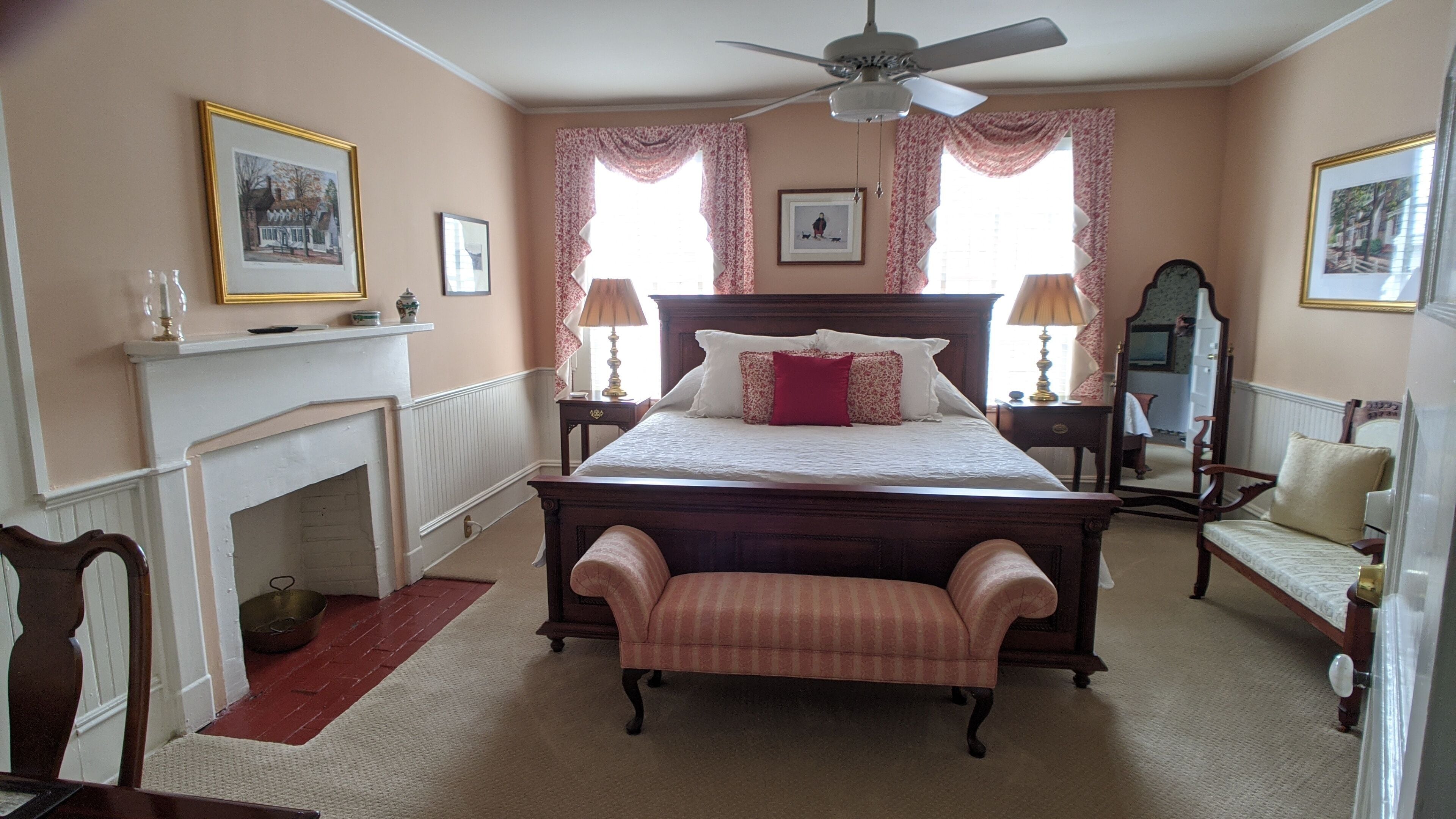 A bedroom with a four-poster bed, a fireplace, a bench, a mirror, and two lamps.