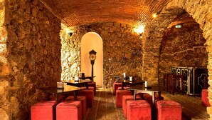 Interior com paredes de pedra, mesas e assentos acolchoados vermelhos.
