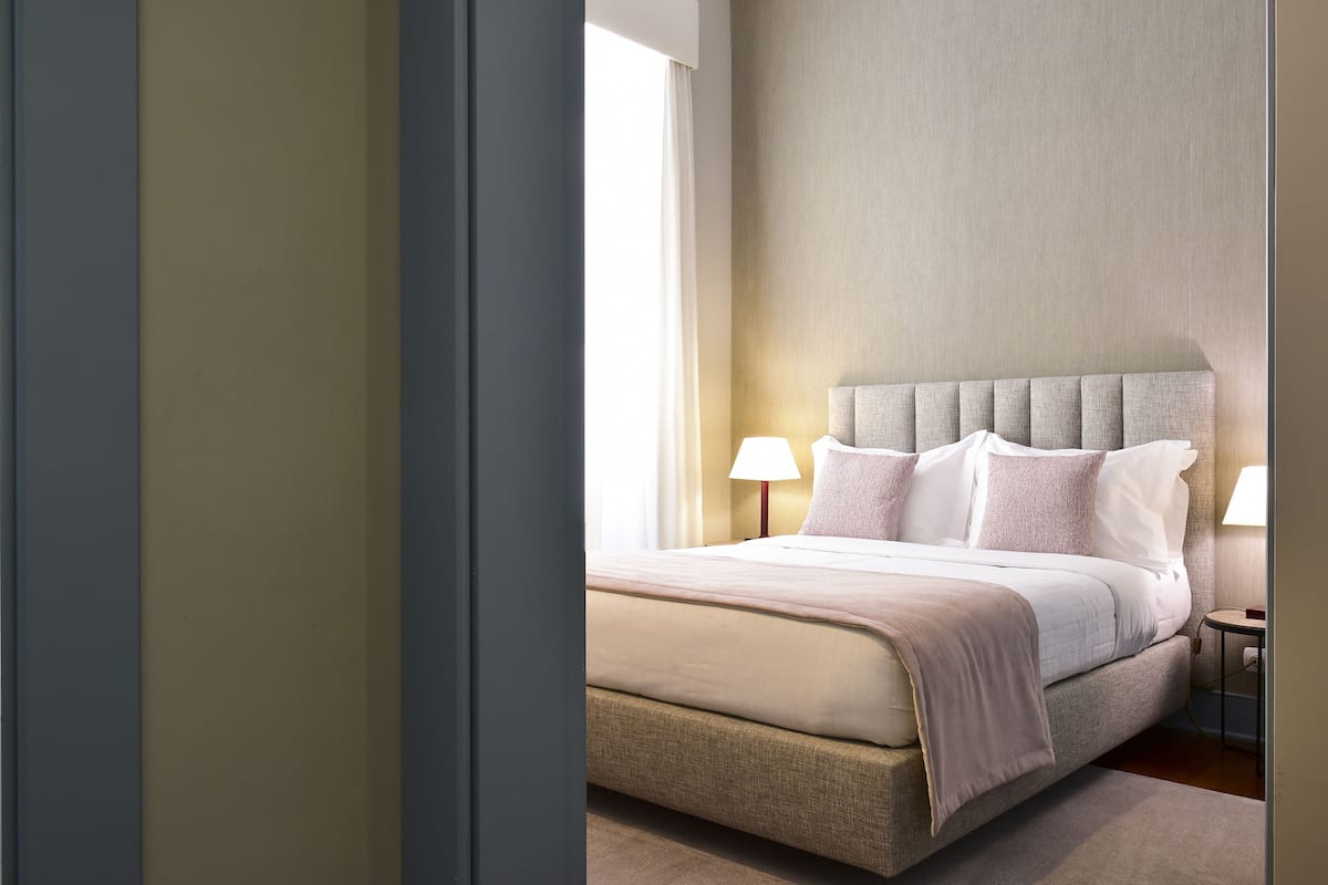Una habitación de hotel moderna con una cama grande, dos lámparas de noche y vistas al exterior.