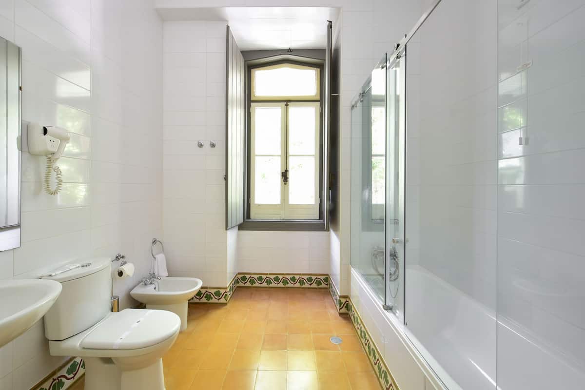 Baño con inodoro, bidé y bañera. Hay una ventana sobre el inodoro y una zona de ducha a la derecha.