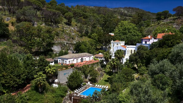 Uma propriedade numa encosta com piscina, edifícios brancos e vermelhos e vegetação exuberante.