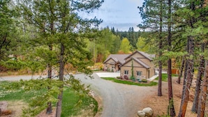 A two-story house with a stone foundation, surrounded by a forested area with tall pine trees. - Evergreen Mountain Lodge (Cle Elum)