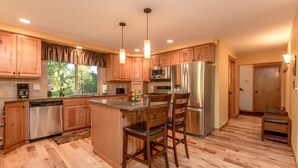 A kitchen with wooden cabinets, stainless steel appliances, a central island with bar stools, and a window with a view of trees. - Evergreen Mountain Lodge (Cle Elum)
