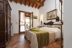 A bedroom with a bed, a nightstand, a lamp, a painting, and a wooden ceiling. - Agriturismo La Rombaia (Castiglione della Pescaia)