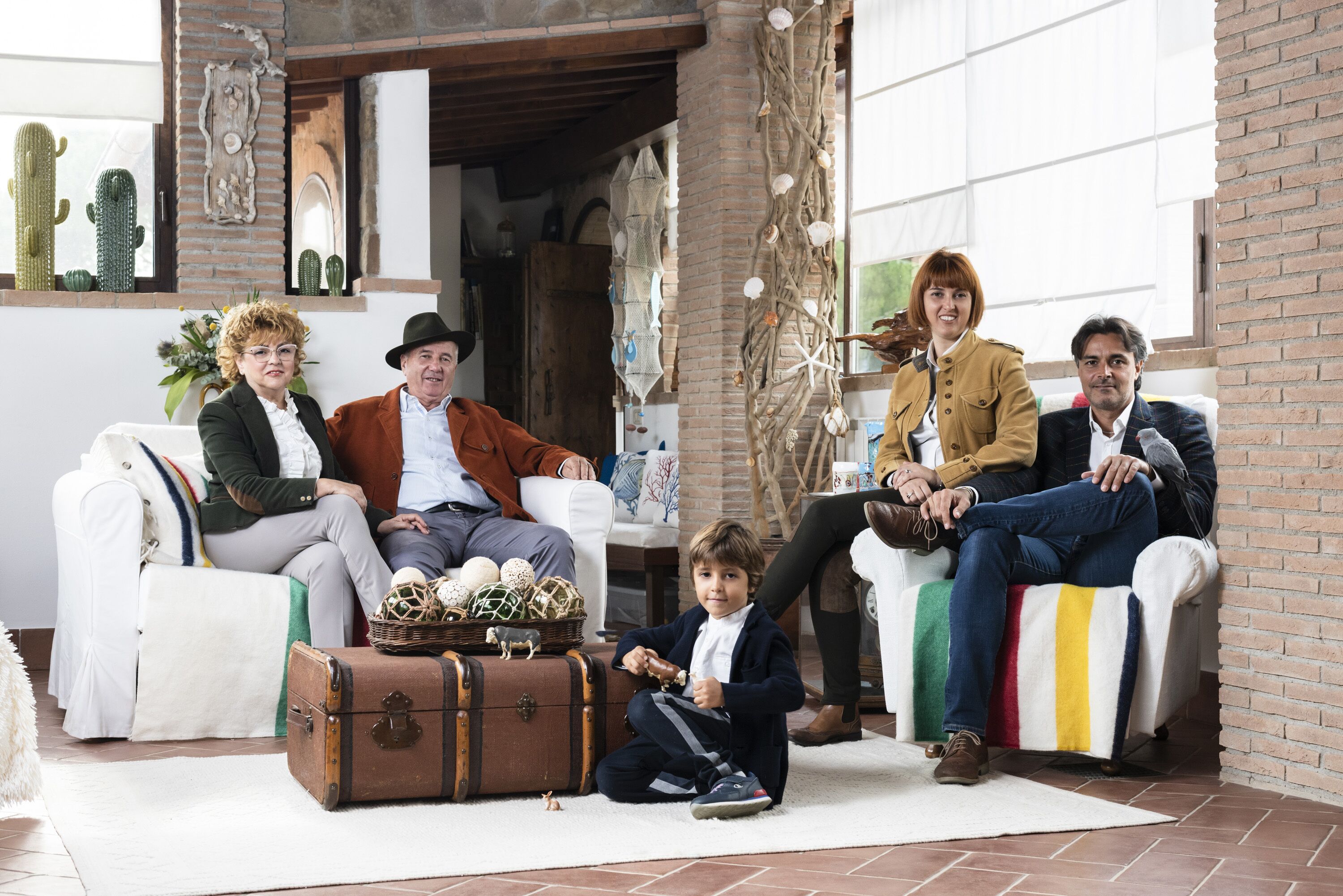 A family sitting on a white couch with a suitcase and a basket of eggs in front of them.