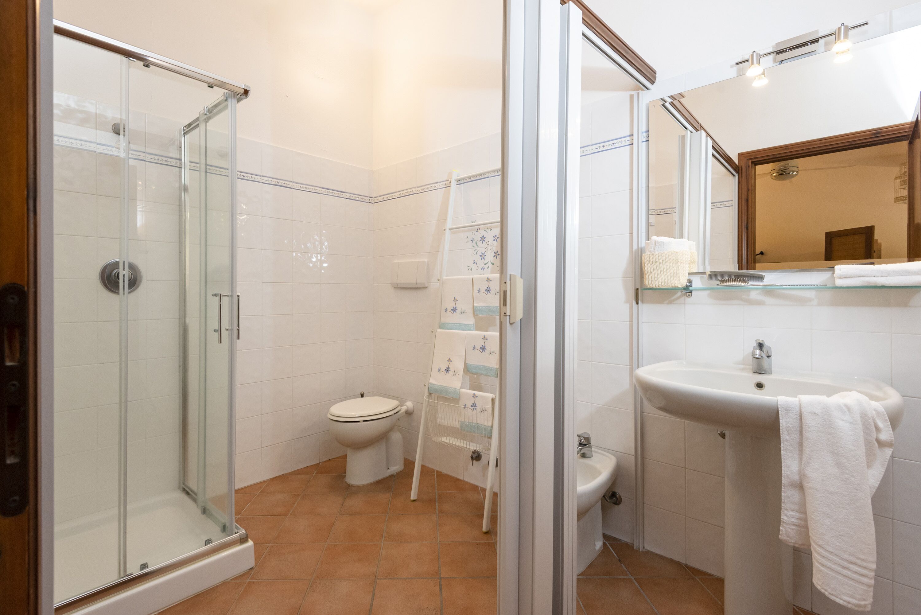 A bathroom with a glass shower enclosure, a toilet, a sink with a towel, and a mirror.