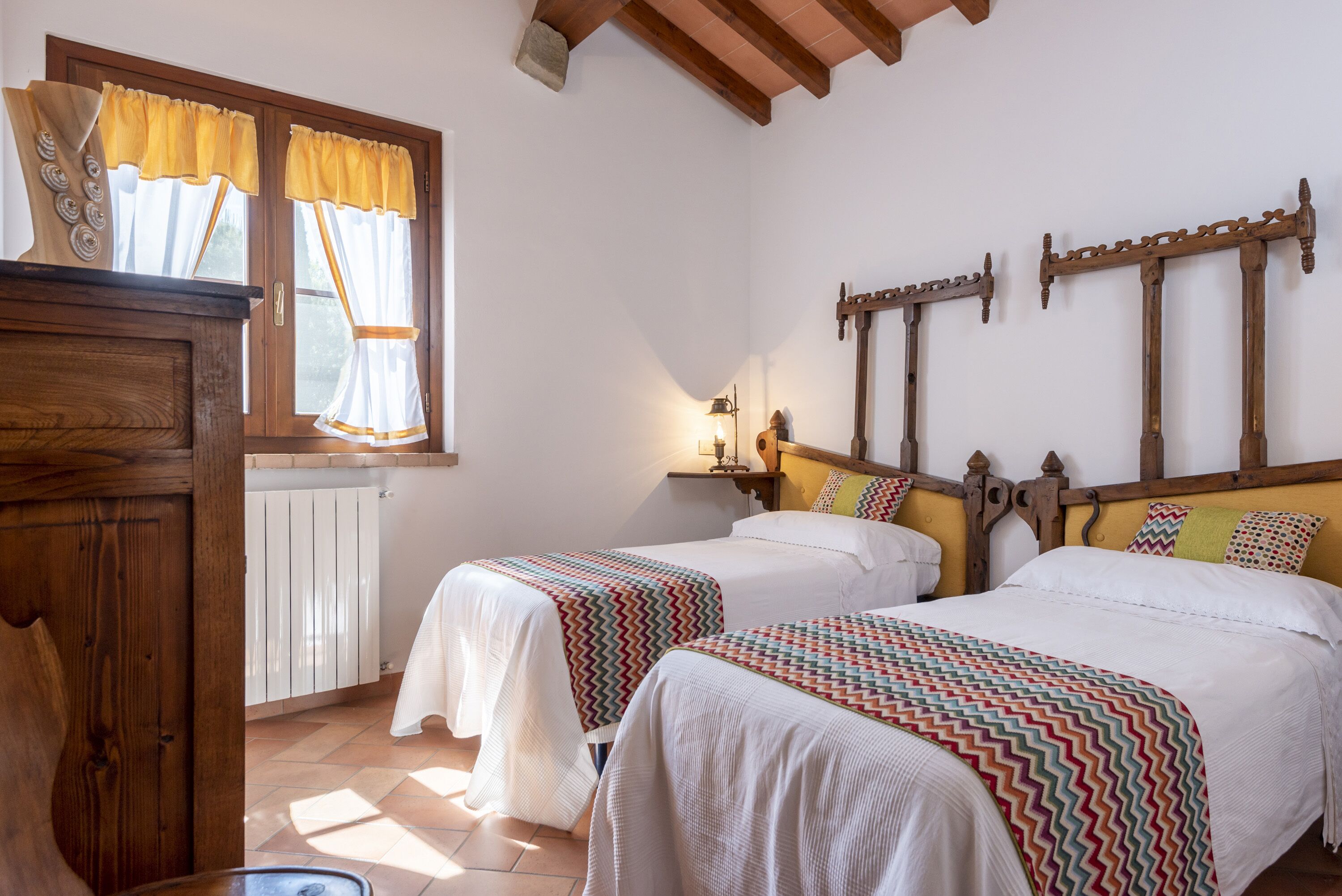 Une chambre avec deux lits, des têtes de lit en bois, une commode en bois et une fenêtre avec des rideaux.