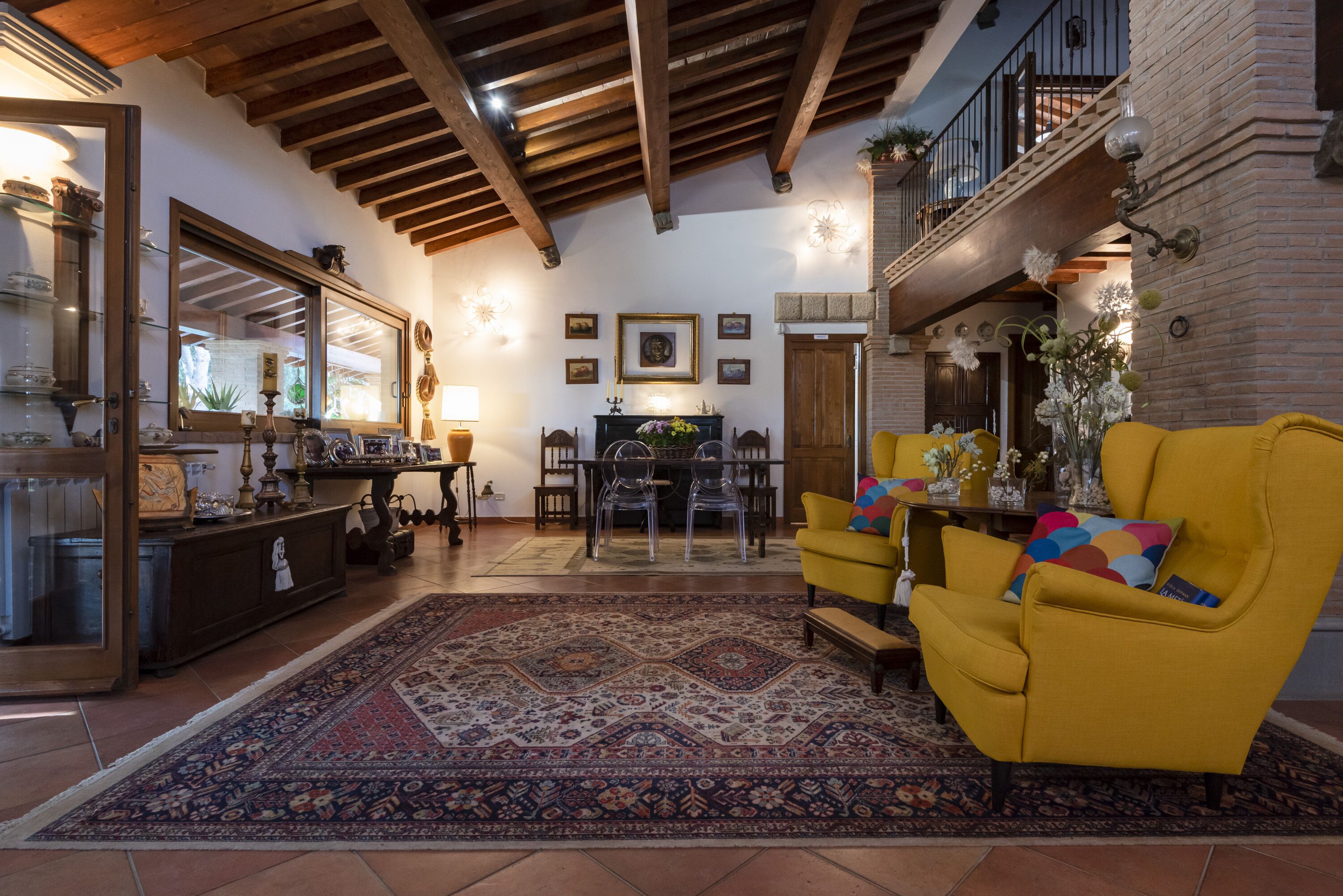 Un salón espacioso con un sillón amarillo, una alfombra estampada y una zona de comedor con una mesa y sillas.