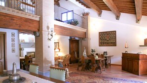 A spacious living area with a high ceiling, wooden beams, a balcony, and a patterned rug. - Agriturismo La Rombaia (Castiglione della Pescaia)