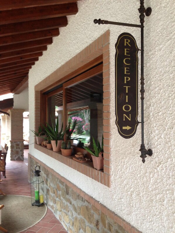 Un letrero de recepción con una flecha indicadora, una ventana con plantas en macetas y una pared de piedra.