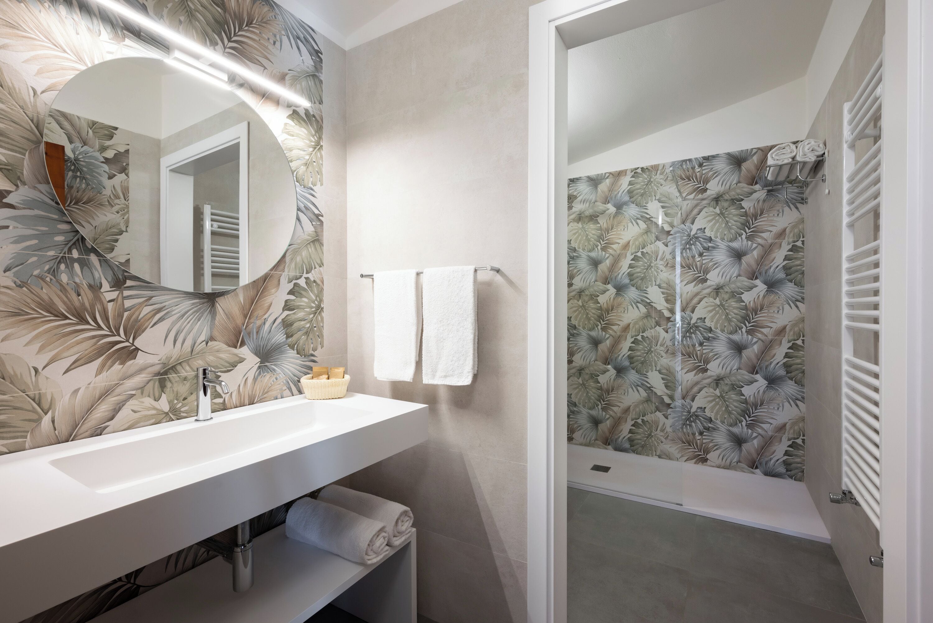 A bathroom with a white sink, a mirror, and a shower with a floral wallpaper.