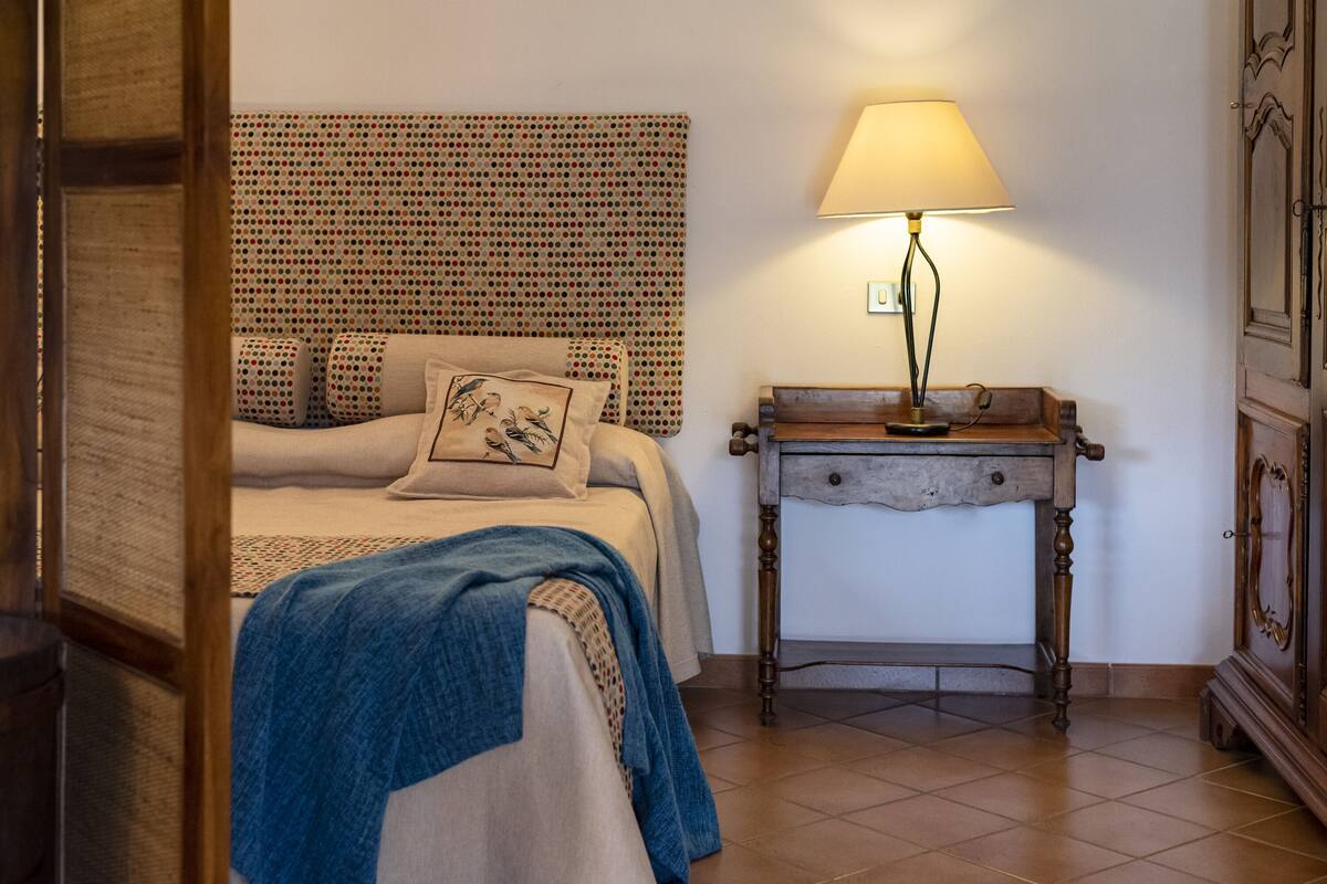 Een slaapkamer met een bed, nachtkastje, lamp en hoofdbord met stippen.