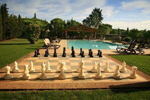 A large outdoor chessboard set up on a patio with a pool and lounge chairs in the background. - Agriturismo La Rombaia (Castiglione della Pescaia)