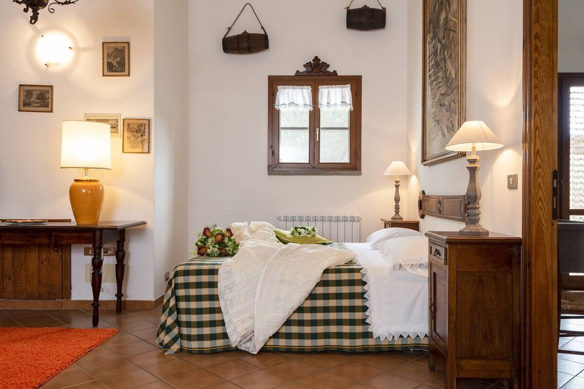 Een slaapkamer met een geruite sprei, twee bedlampjes, een radiator en een houten nachtkastje.