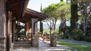A stone building with a covered patio, outdoor seating, and a view of trees and mountains. - Agriturismo La Rombaia (Castiglione della Pescaia)