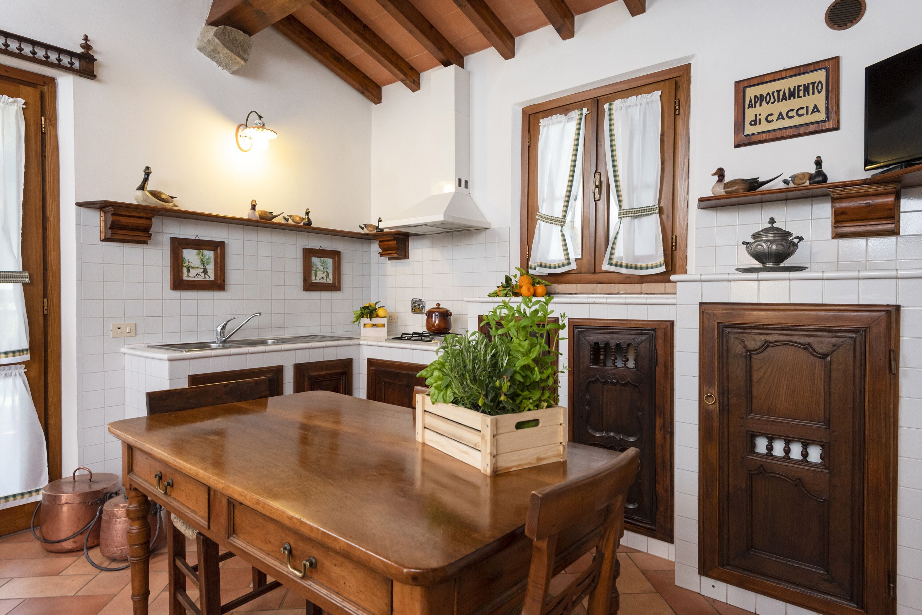 A kitchen with a wooden table, white tiles, and a wooden cabinet.