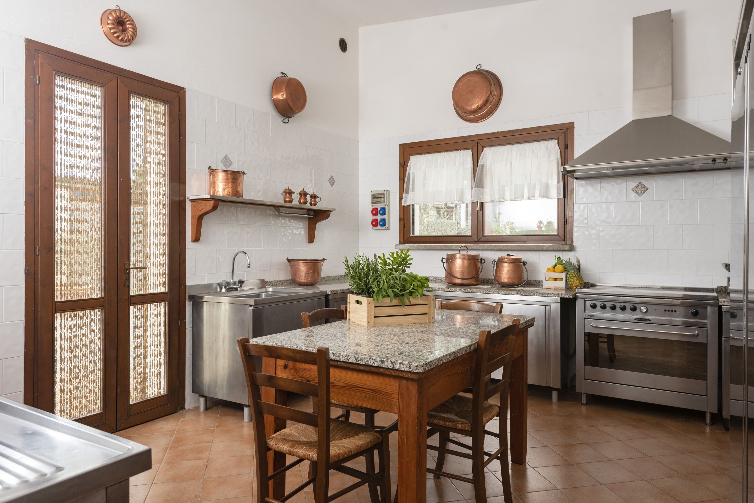 Une cuisine dotée d’un plan de travail en granit, de chaises en bois, d’un évier en acier inoxydable, de casseroles en cuivre et d’une cuisinière.