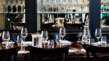 L’intérieur d’un restaurant présente de nombreuses tables dressées pour le service, un présentoir à vin contenant différentes bouteilles et un mur miroitant qui reflète l’espace réservé aux convives.