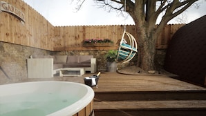 Un bain à remous, une terrasse en bois, un fauteuil suspendu, un mur de pierres et une clôture en bois.