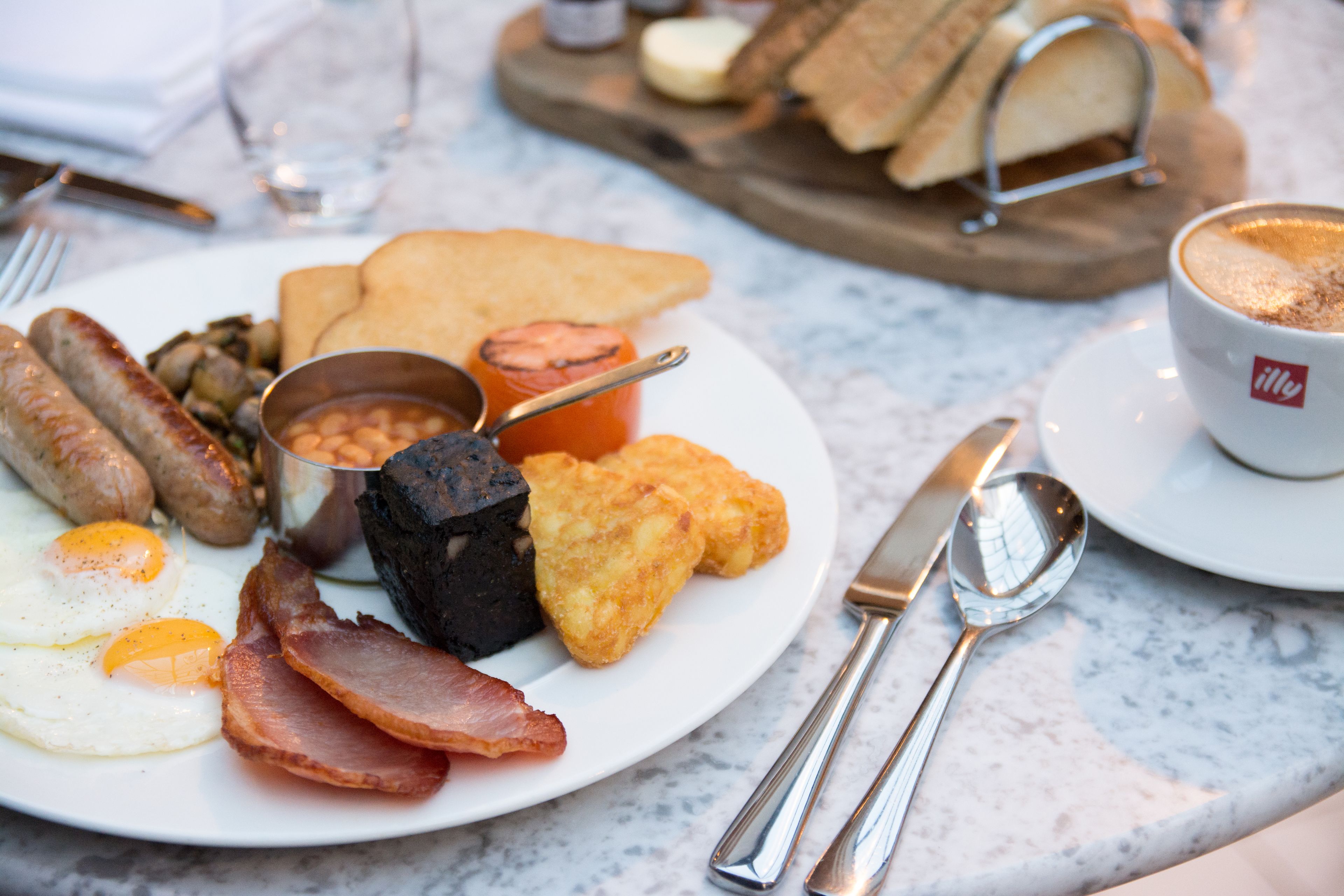 A breakfast plate with eggs, sausages, bacon, beans, toast, and a cup of coffee.