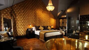 Um quarto luxuoso com cabeceira estofada, uma cama grande, uma banheira dourada e um candelabro.