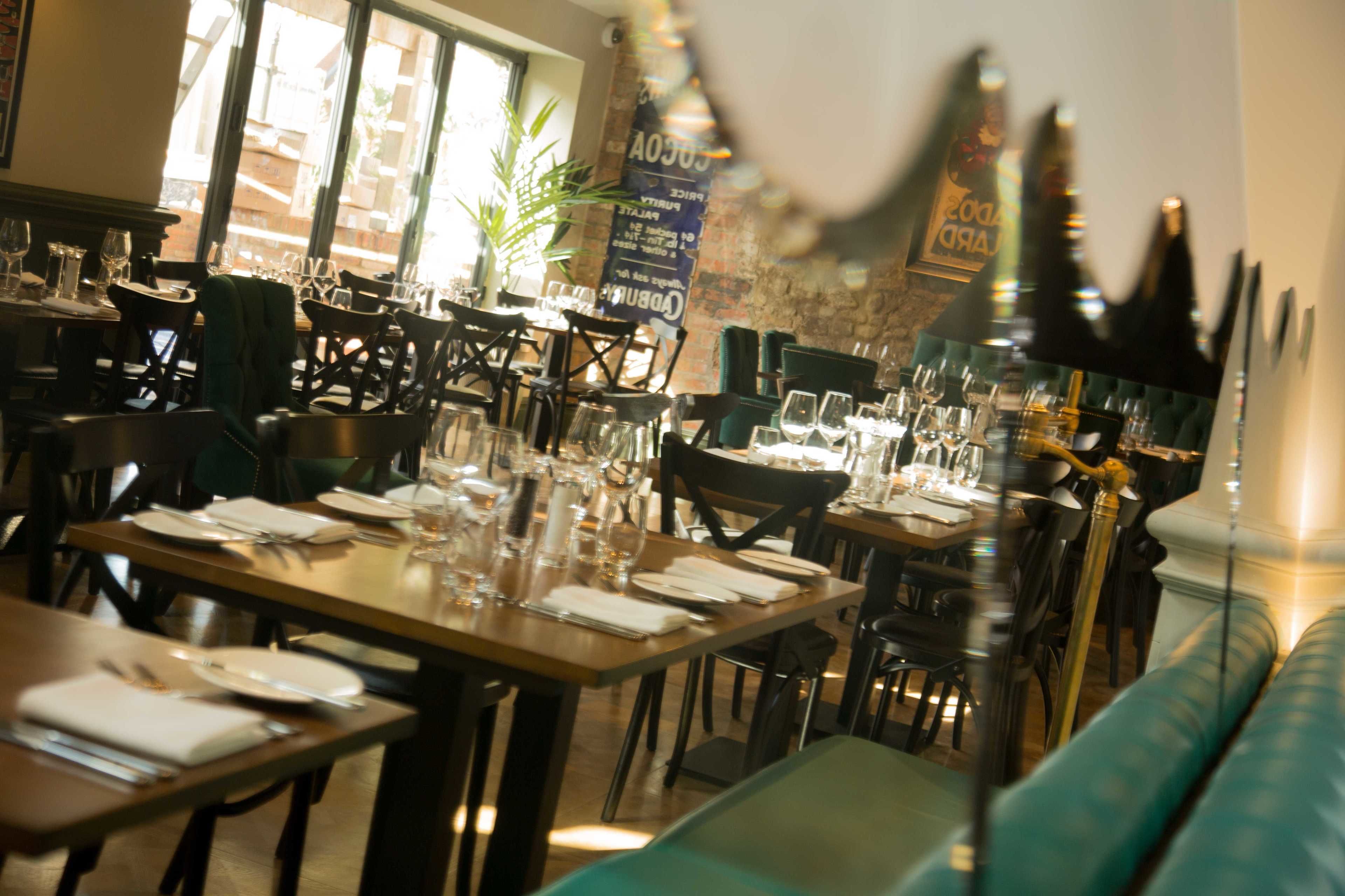A restaurant with tables set for dining, chairs, and a green cushioned bench.