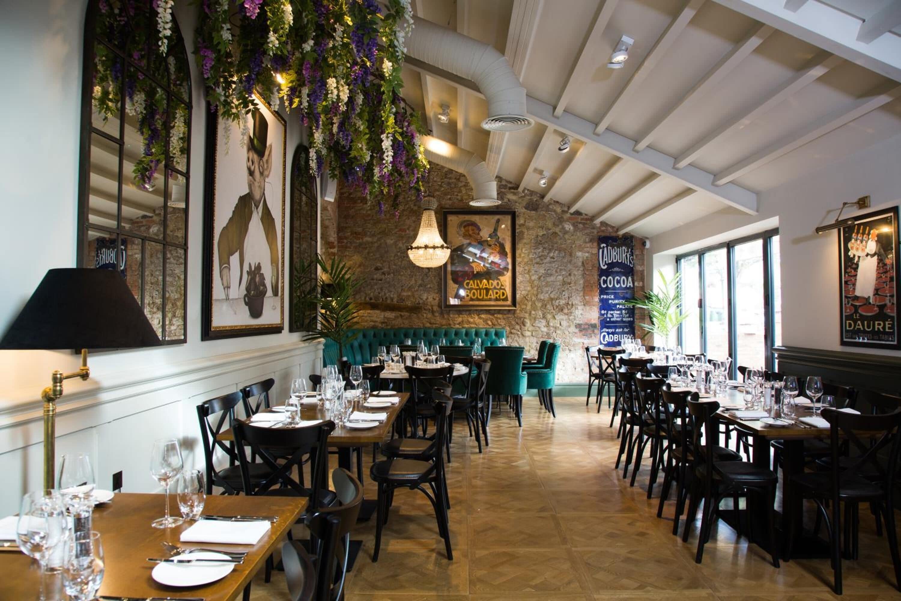 A restaurant with long wooden tables, black chairs, and hanging floral decorations.