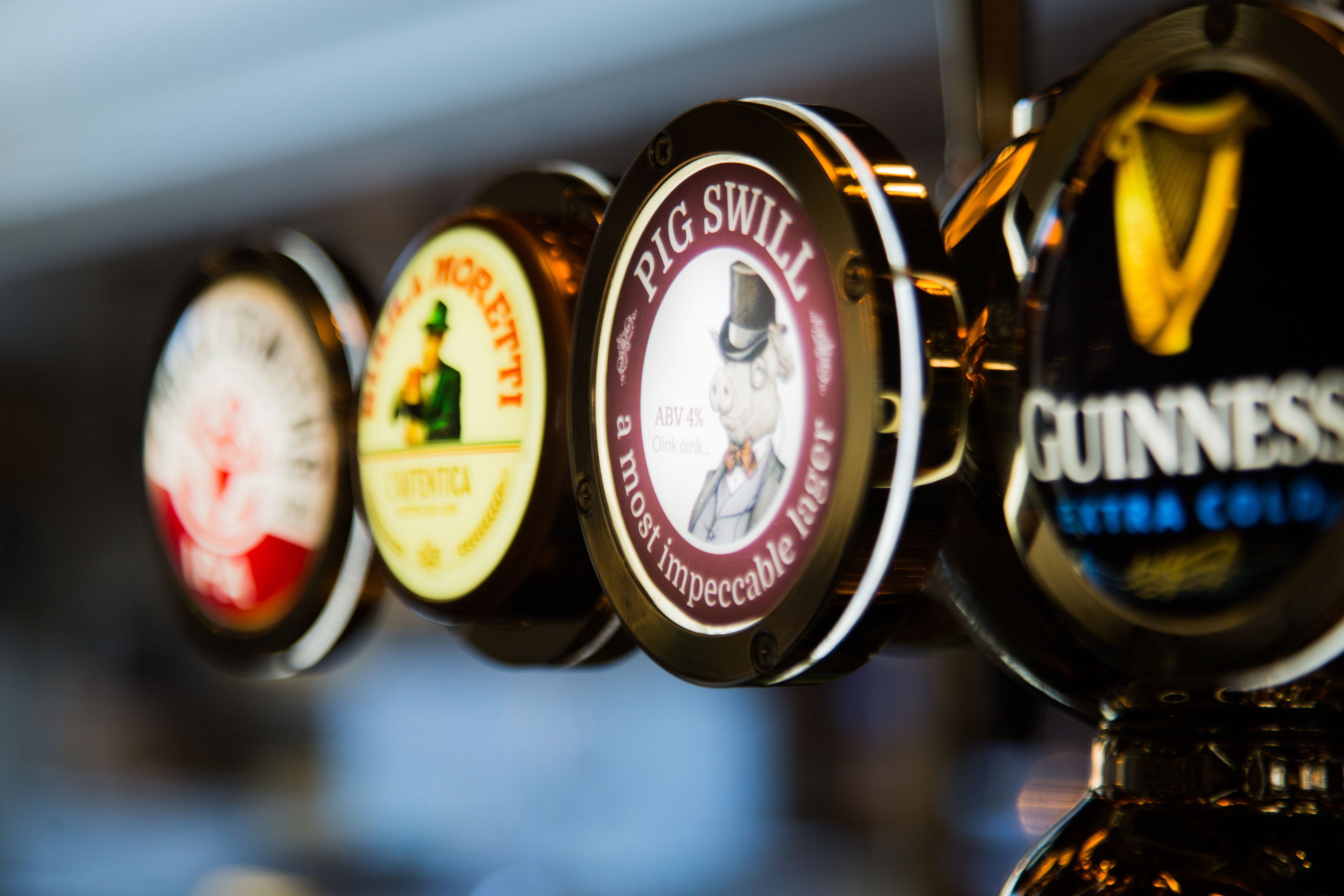 Una hilera de grifos de cerveza con etiquetas que incluyen marcas como Guinness y Pig Swill.