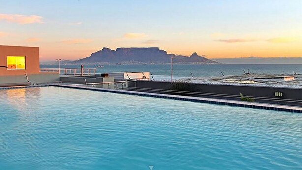 Piscina con vistas a una montaña y al océano al atardecer.