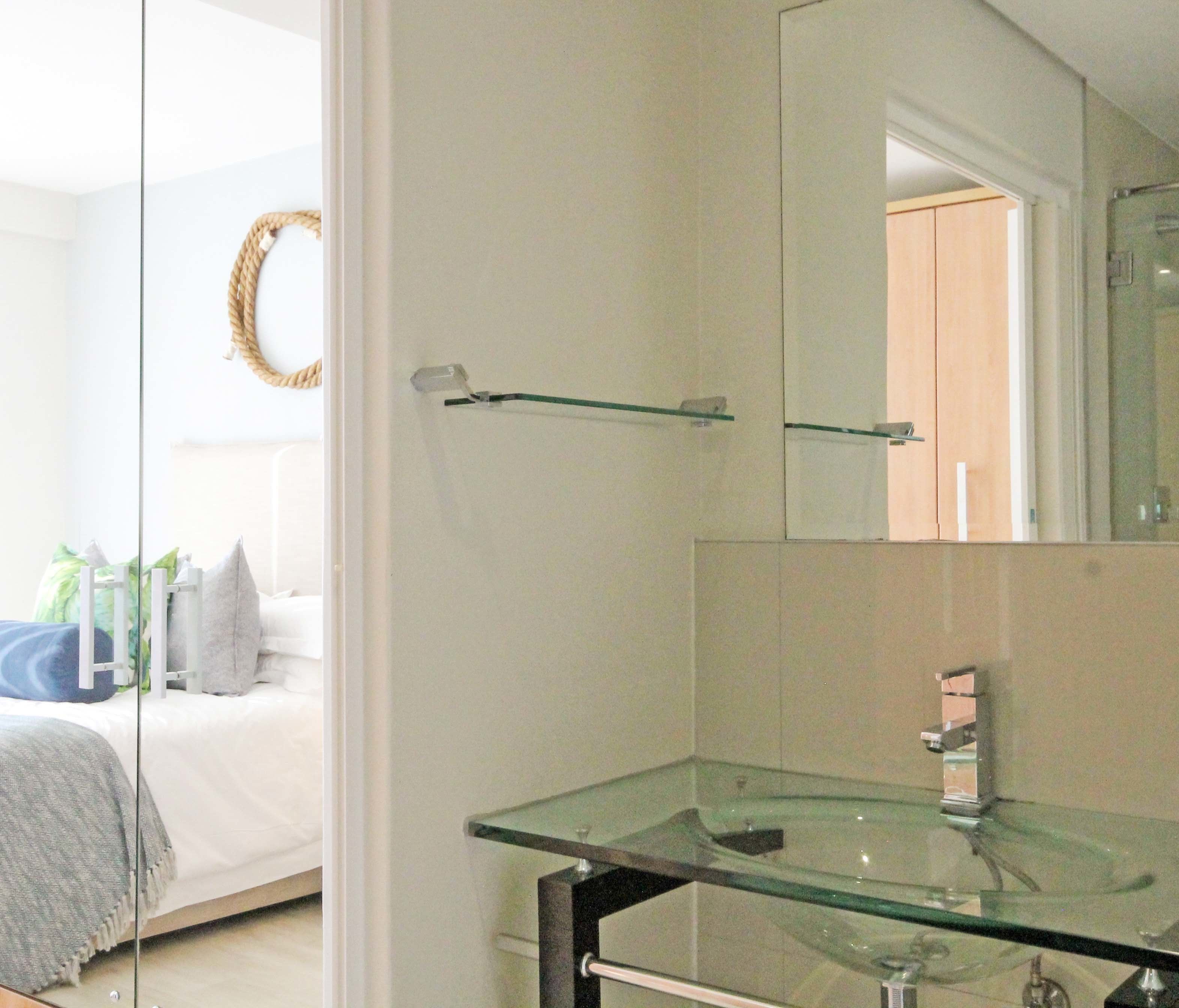A bathroom with a glass sink, a mirror, and a towel rack.