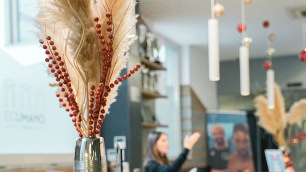 Un mostrador de recepción con un jarrón decorativo de plumas de plumerillo y bayas rojas.