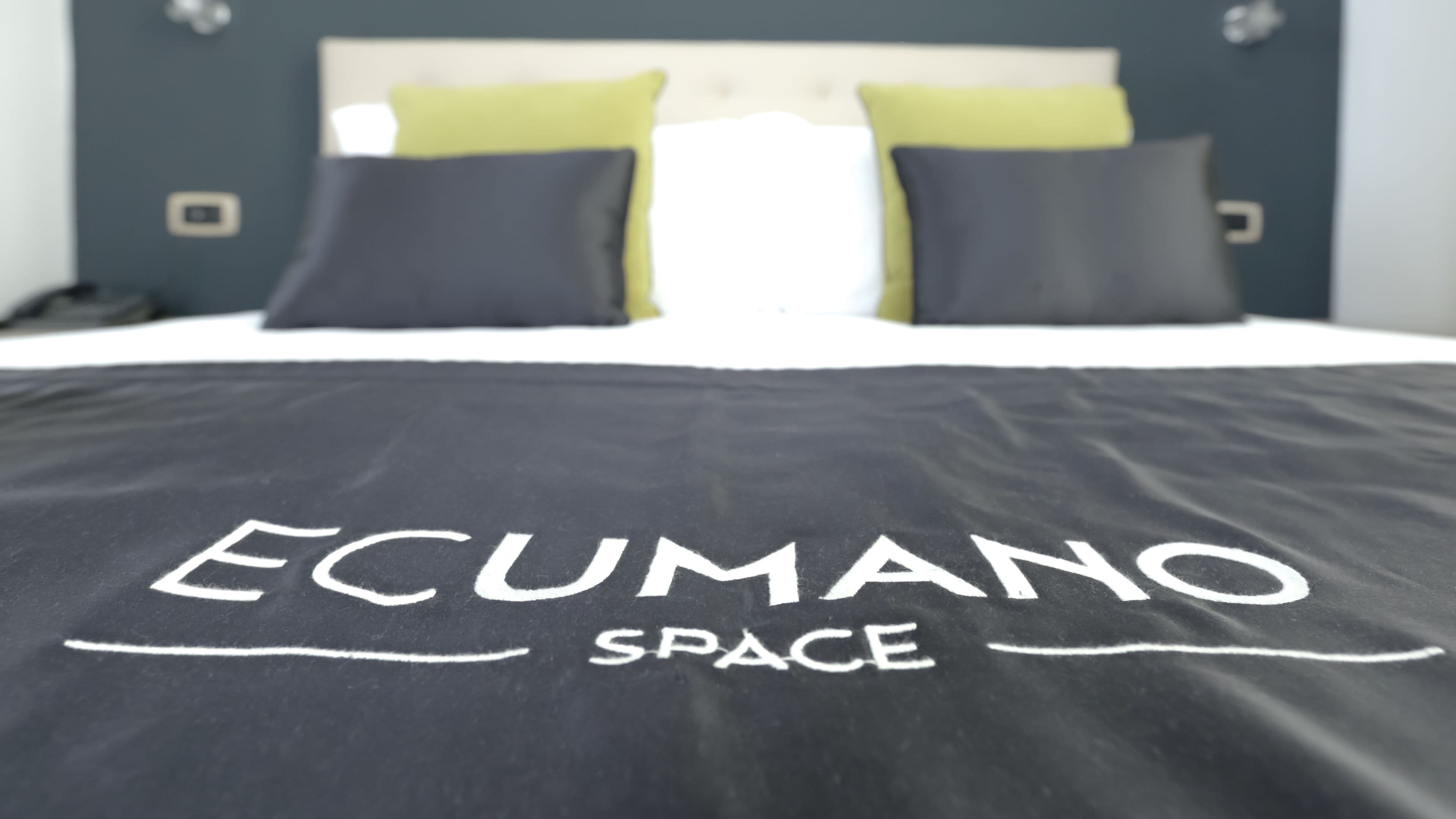 Ein Bett mit einer schwarzen Bettdecke, auf der "ECUMANO SPACE" steht.