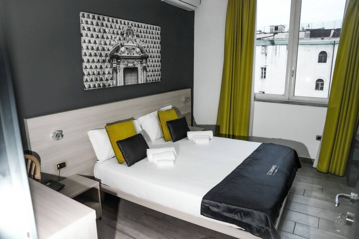 Habitación de hotel con una cama grande, un escritorio con silla, una obra de arte en la pared y una ventana con cortinas.