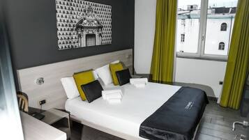 Habitación de hotel con una cama grande, un escritorio con silla, una obra de arte en la pared y una ventana con cortinas.