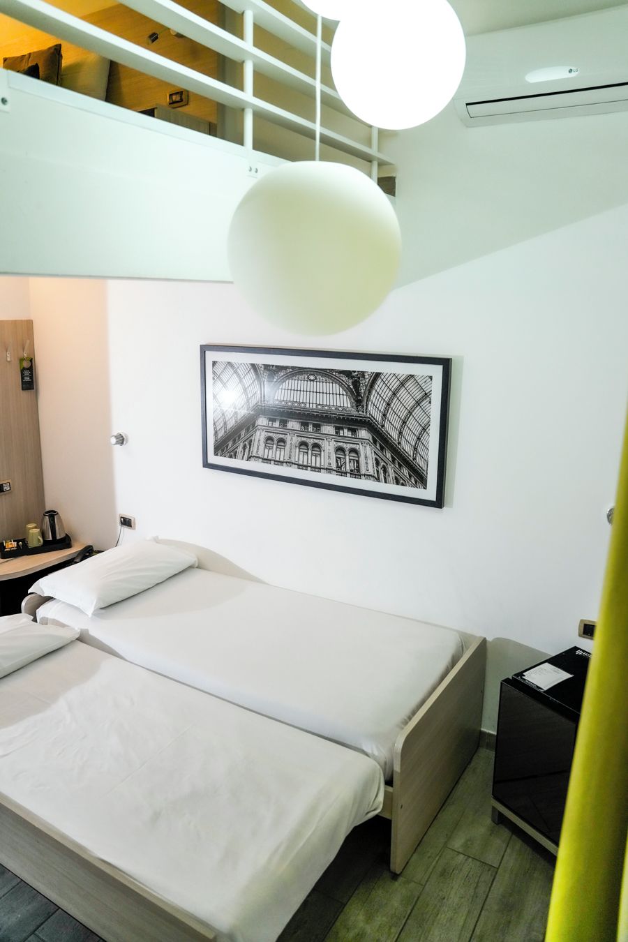 Et moderne hotelværelse med en seng, et indrammet billede af en bygning og en loftslampe.