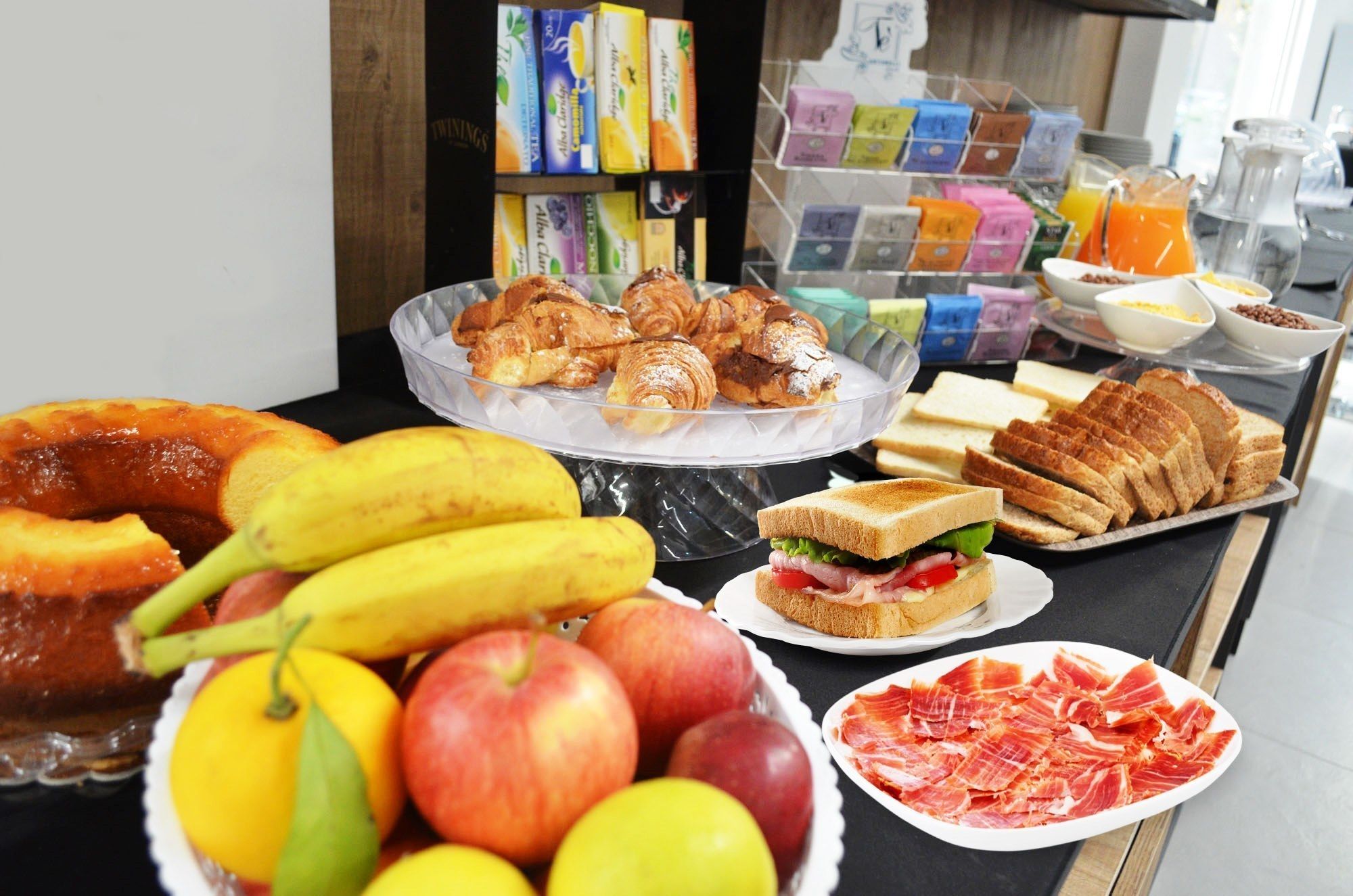 Een ontbijtbuffet met croissants, belegde broodjes, fruit en diverse drankjes.
