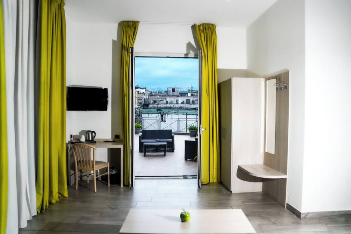 Habitación de hotel moderna con balcón, zona de comedor y televisor en la pared.