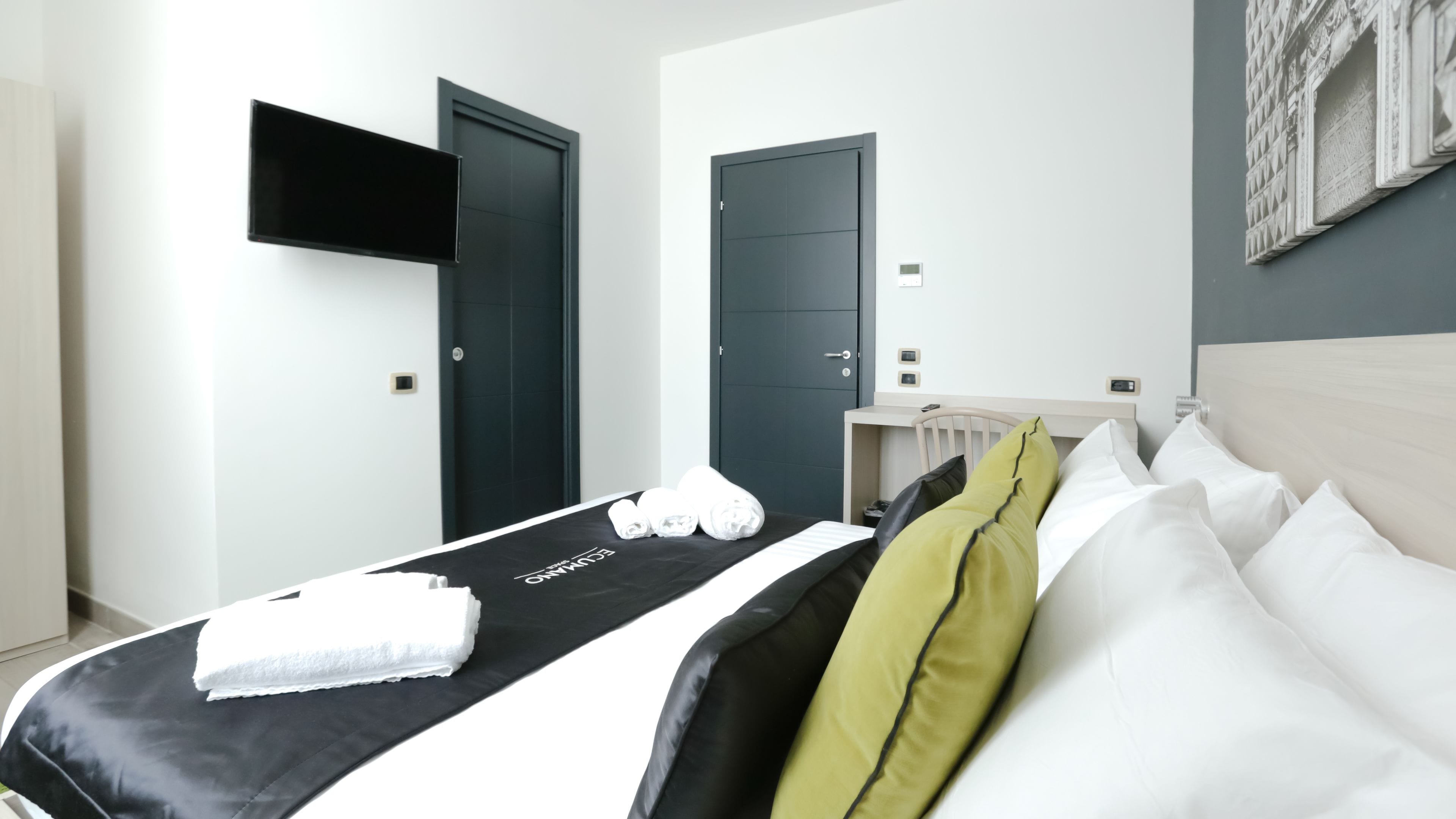 Ein Hotelzimmer mit Bett, Flachbildfernseher an der Wand, Holz-Kopfstütze und Tür mit Griff.