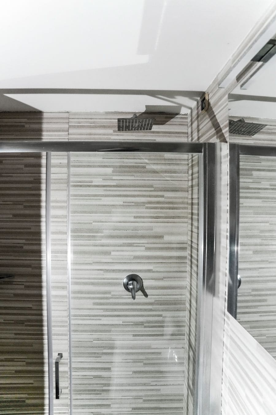 A modern bathroom with a striped tile wall, a metallic faucet, and a glass door.