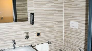 Un baño moderno con lavamanos, espejo y váter blancos. Las paredes tienen un diseño que imita la madera, y a la derecha se encuentra la zona de ducha.